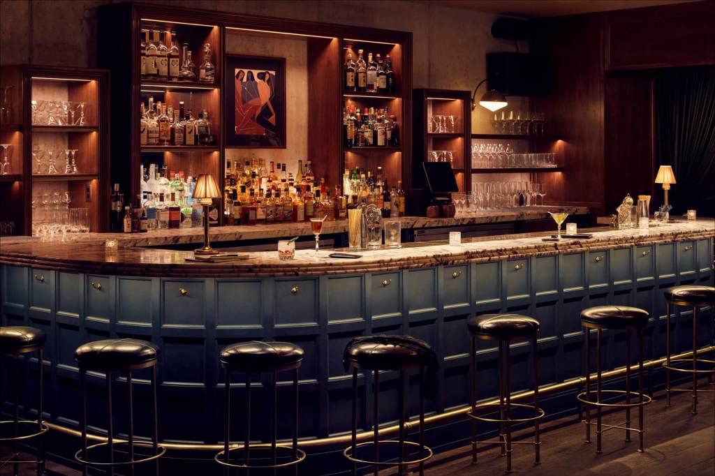 The shelving behind the bar is wooden and houses lots of different bottles and glassware