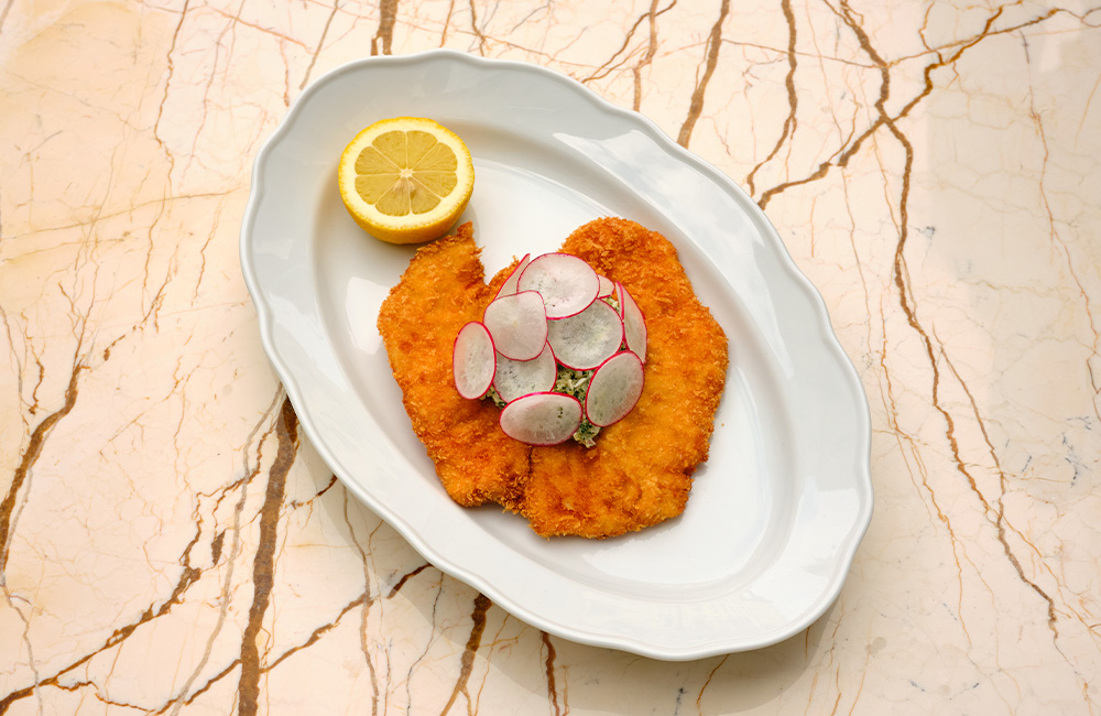 chicken schnitzel served with chopped radish and half a lemon.